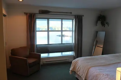 a bedroom with a bed and a chair and a window at Siennas Harbour House in Tofino