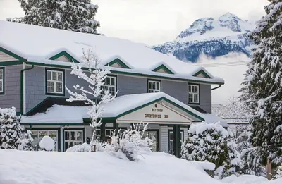 a house covered in snow with mountains in the background at Courthouse Inn Revelstoke in Revelstoke