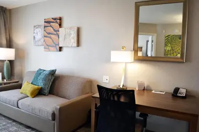 a hotel room with a desk and a couch and a mirror at Staybridge Suites - Red Deer North by IHG in Red Deer