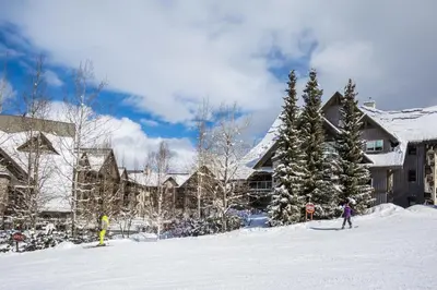 two people skiing in the snow in front of a lodge at The Aspens by Whistler Premier in Whistler