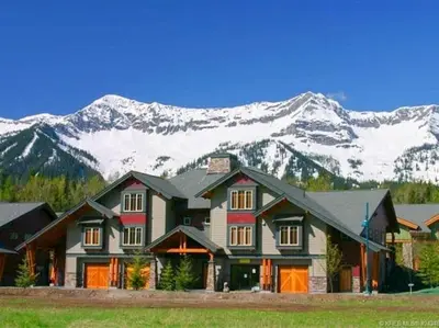 a large house with snow covered mountains in the background at Pinnacle Ridge Condos by Fernie Central Reservations in Fernie