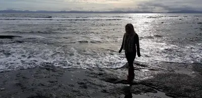 a woman walking on the beach near the water at Newfie Seaside Retreat in Port Renfrew