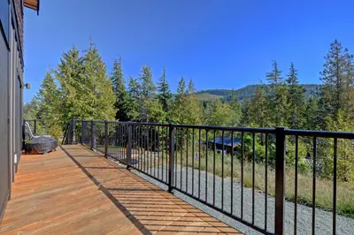 a balcony with a black fence and trees at Newfie Seaside Retreat in Port Renfrew