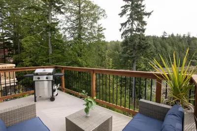 a patio with a grill and chairs on a deck at Le Chalet Waterfront Retreat in Ucluelet
