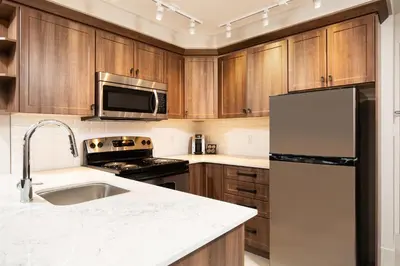 a kitchen with wooden cabinets and a stainless steel refrigerator at Pomeroy Hotel Fort McMurray in Fort McMurray