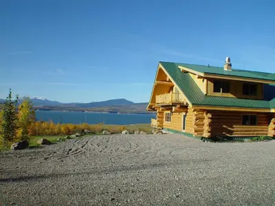 a log cabin with a gravel road next to a lake at Williston Lake Resort in Hudson Hope