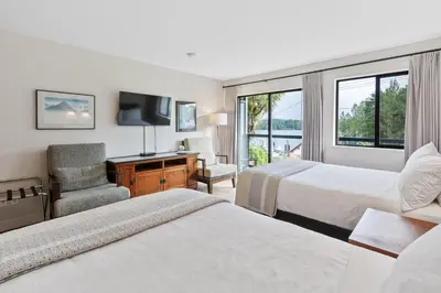a hotel room with two beds and a chair and a window at Tofino Motel Harbourview in Tofino