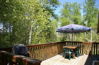 a wooden deck with a table and an umbrella at Creekside Cabin in Fairmont Hot Springs