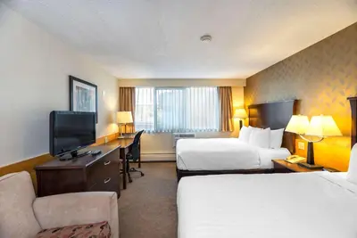 a hotel room with two beds and a desk with a television at Prestige Riverside Lodge Quesnel in Quesnel