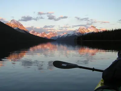 a person in a kayak on a lake with mountains at Sundance Suite - Beautiful Condo With Open Pool And Hot Tub in Canmore