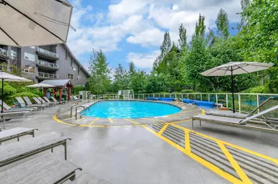 a swimming pool with benches and an umbrella at The Best ski-in/ski-out at The Aspens in Whistler