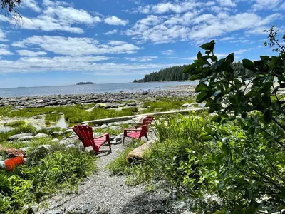 two red chairs sitting on a beach near the water at So Damn Lucky Glamping in Ucluelet