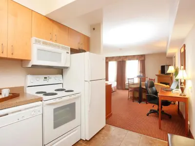 a kitchen with white appliances and a living room at Stonebridge Hotel Dawson Creek in Dawson Creek