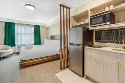 a hotel room with a bed and a kitchen with a refrigerator at Velora Hinton, an Ascend Collection Hotel in Hinton
