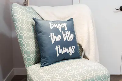 a pillow that says enjoy the little things sitting on a chair at Modern Executive Suite I Complimentary Netflix & Parking! in Edmonton