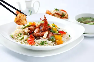 a bowl of noodles with shrimp and vegetables on a table at Pomeroy Hotel Fort St. John in Fort Saint John