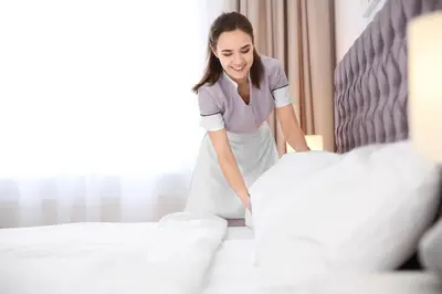 a woman making a bed in a hotel room at Pomeroy Inn & Suites Fort St. John in Fort Saint John
