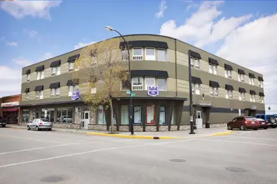 a building on a street with cars parked in a parking lot at Central Suite Hotel in Lloydminster
