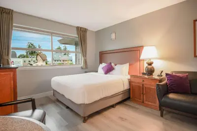 a bedroom with a bed and a chair and a window at Coast Parksville Hotel in Parksville