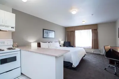 a hotel room with a white bed and a kitchen at Sandman Hotel & Suites Williams Lake in Williams Lake
