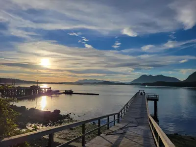 a dock with the sun setting over a lake at Schooner Motel in Tofino