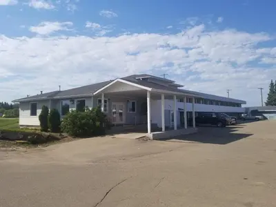 a white building with a car parked in a parking lot at Super 8 by Wyndham Smoky Lake in Smoky Lake