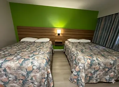 two beds in a hotel room with green walls at Quesnel Inn in Quesnel