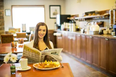 a woman sitting at a table reading a newspaper at Service Plus Inns & Suites Drayton Valley in Drayton Valley