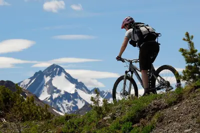 a person riding a bike on a hill with a snow covered mountain at Tyax Lodge & Heliskiing in Gold Bridge