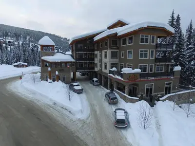 a large building with cars parked in the snow at Kookaburra Lodge #202 By Bear Country in Sun Peaks