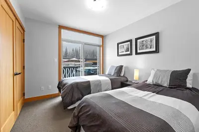 a bedroom with two beds and a window with a boat outside at Kookaburra Lodge #203 By Bear Country in Sun Peaks