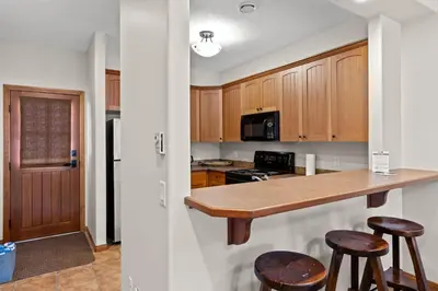 a kitchen with wooden cabinets and a counter with stools at Trails Edge #17 By Bear Country in Sun Peaks
