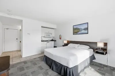 a bedroom with a large white bed and a kitchen at Lillooet Hotel Victoria in Lillooet