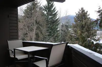 a table and chairs on a balcony with a view of trees at Rainbow Suites by Whistler Retreats in Whistler