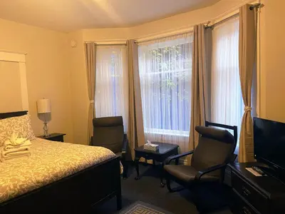 a bedroom with a bed and two chairs and windows at Douglas Guest House in Vancouver
