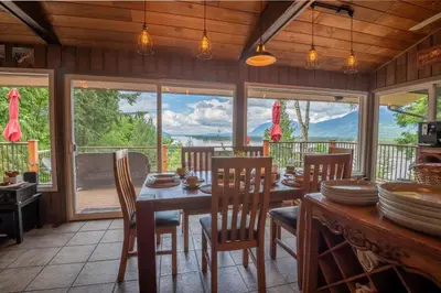 a dining room with a table and chairs and windows at The Fraser River's Edge B&B Lodge in Chilliwack