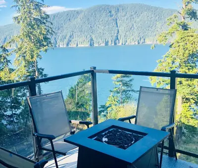 a table and chairs on a balcony with a view of a lake at Sandy Feet Retreat Port Renfrew- Oceanfront 2BR modern cottage in Port Renfrew