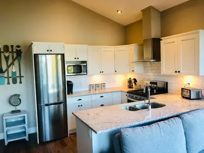 a kitchen with white cabinets and a stainless steel refrigerator at Sandy Feet Retreat Port Renfrew- Oceanfront 2BR modern cottage in Port Renfrew