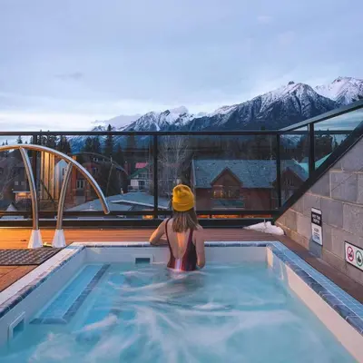 a woman in a swimming pool with mountains in the background at Basecamp Suites Canmore in Canmore