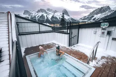 two women sitting in a swimming pool in the snow at Basecamp Suites Canmore in Canmore