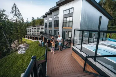 two people standing on a deck next to a house with a swimming pool at Basecamp Resorts Revelstoke in Revelstoke