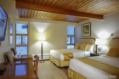 a hotel room with two beds and a desk and windows at Grizz Hotel in Revelstoke