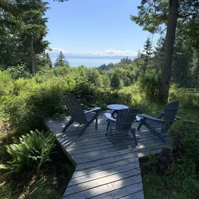 a wooden deck with four chairs and a table at Forest by the Sea Rentals in Merville