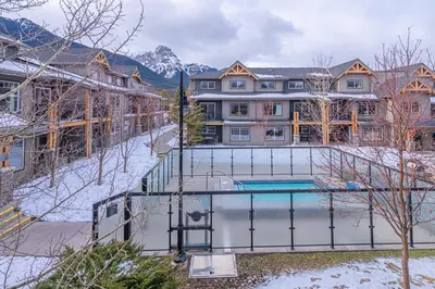 a large house with a swimming pool in the snow at Mountain View Escape - Copperstone 2BR & Hot Tub in Canmore