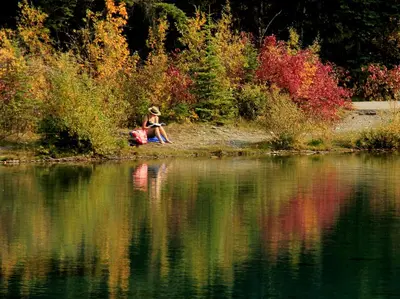 a woman sitting on the shore of a body of water at Anniversary and Honeymoon 1 Bedroom Suite 168 in Canmore