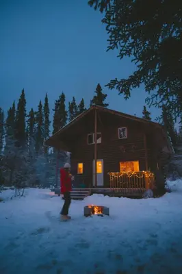 a person standing in the snow in front of a log cabin at Little Atlin Lodge in Tagish