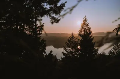 a sunset over a lake with trees in the foreground at The Sanctuary Retreat Salt Spring Island in Salt Spring Island
