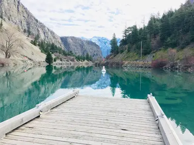 a wooden dock on a river with a boat in the water at Hotel Deoro in Lillooet