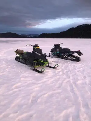 two snowmobiles are parked on a snow covered field at Lac Des Roches Resort in Bridge Lake