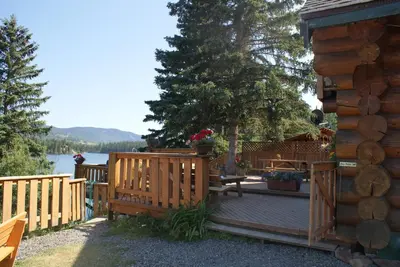 a wooden deck with a bench and a house at Lac Des Roches Resort in Bridge Lake